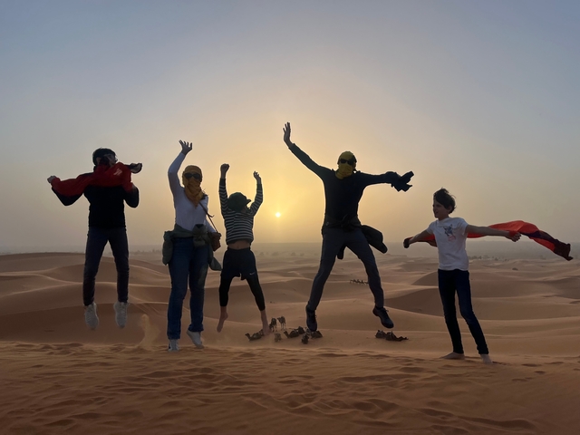       Group of people jumping in the desert at sunrise.
  