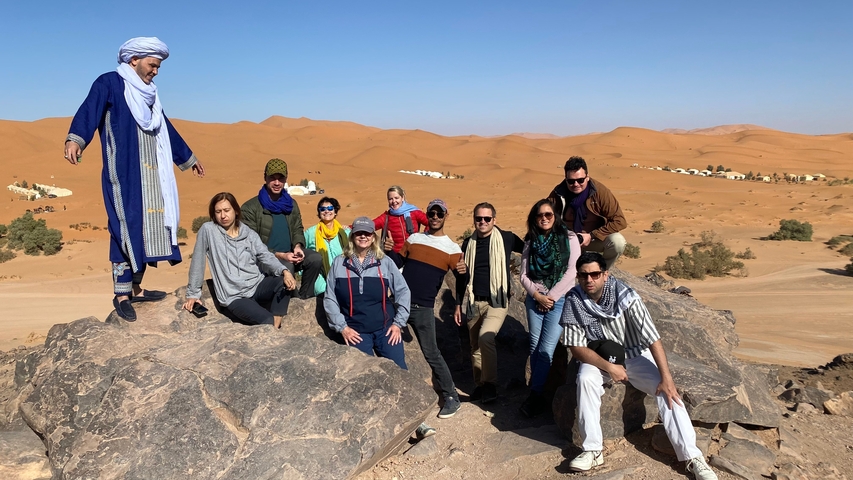       Tour group posing on rocks with dunes in the background.
  