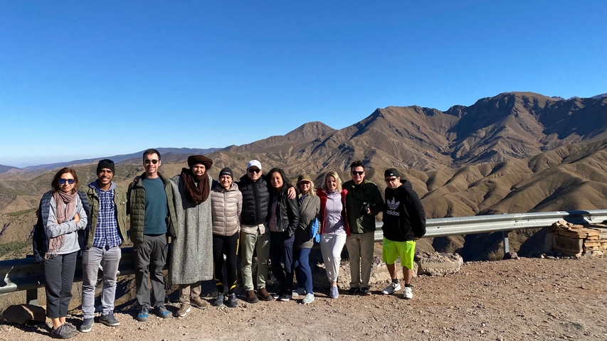 Group posing on a mountain road overlooking a range.