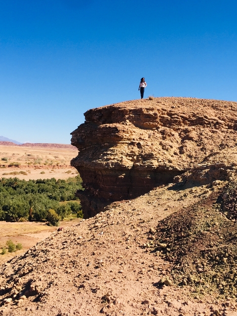       Cliff overlooking a green valley with a blue sky.
  