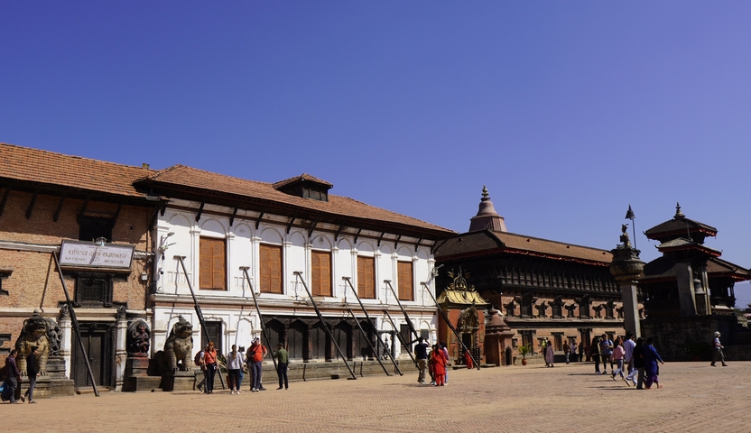       Open square with historical buildings and some tourists walking around.
  