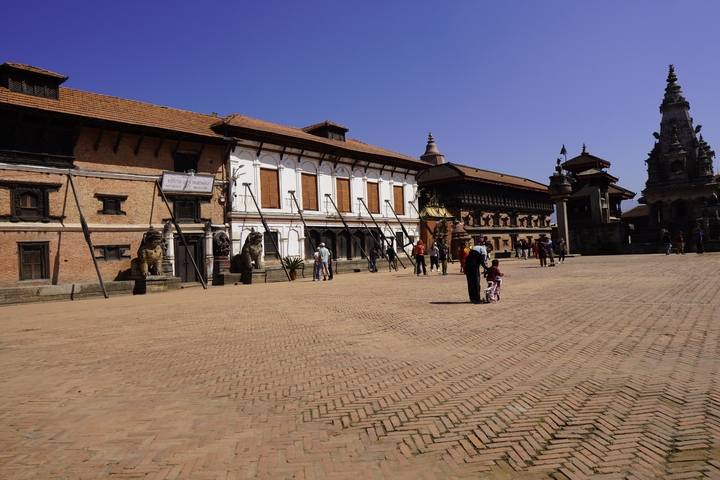       Open square with historical buildings, tourists are exploring.
  