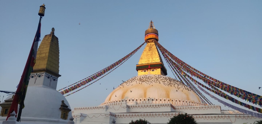       Boudhanath Stupa with prayer flags and a clear sky.
  