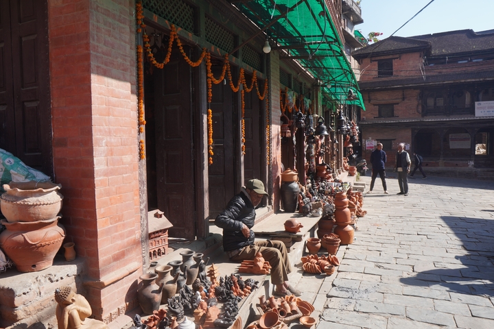       A person working with pottery at a street-side stall.
  