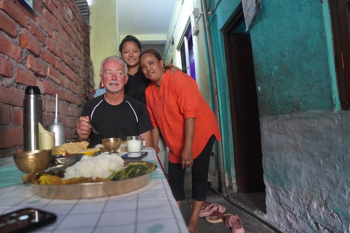       Two people posing with a local in a narrow alleyway with food.
  