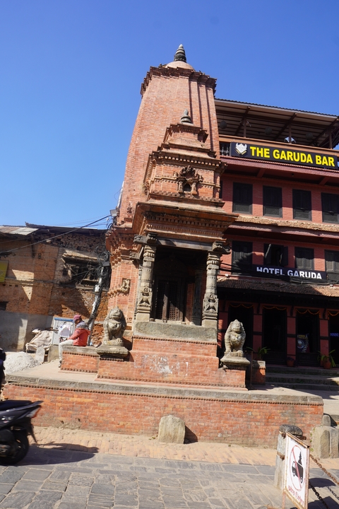       A small ornate structure beside a red brick building.
  