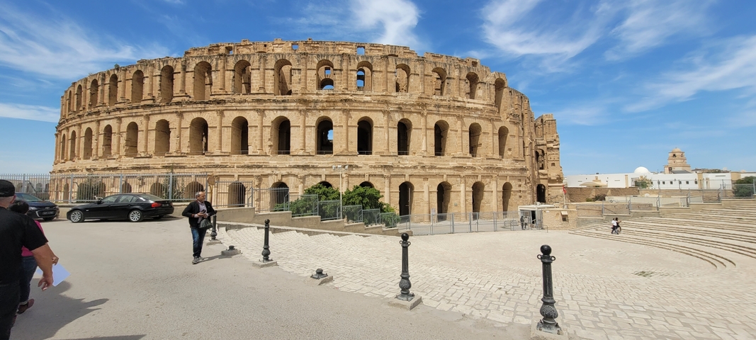       Colosseum-like structure with people walking nearby.
  