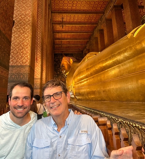 Two men posing with a large reclining Buddha statue.