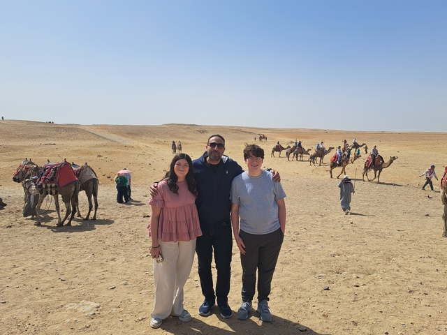 Tourists posing in the desert with camels in the background.