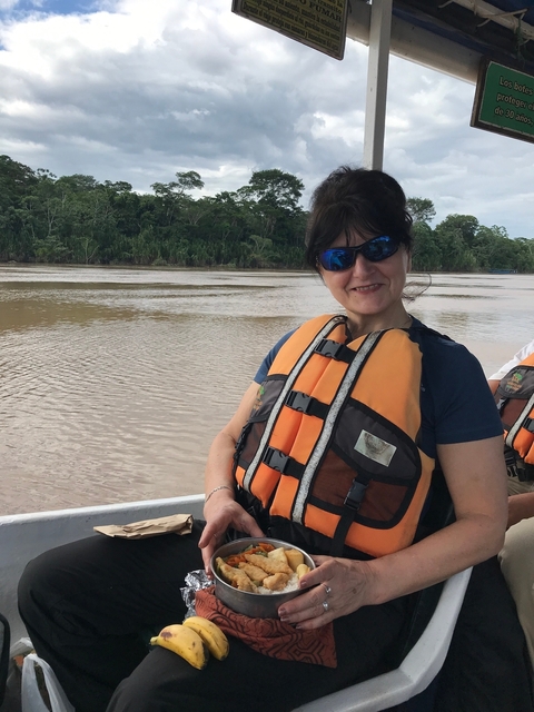      Person in a life jacket on a boat in a river surrounded by lush greenery.
  