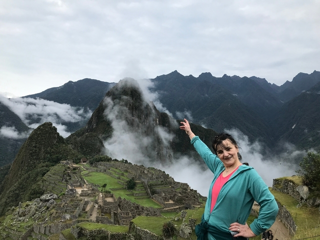       Person pointing at Machu Picchu with mountains and mist in the background.
  