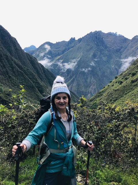       Person wearing a beanie and backpack with mountains and greenery in the background.
  