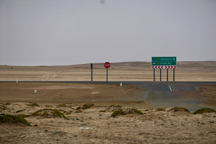A desert crossroads with stop sign and road signs indicating directions to Swakopmund and Henties Bay.