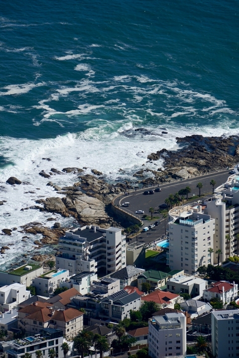 Aerial view of a rocky coastline with crashing waves and an adjacent road.