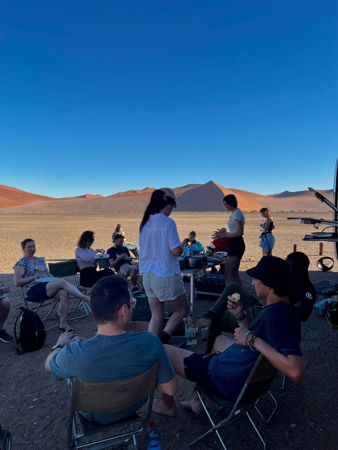      A group of people enjoying a picnic in the desert under a clear blue sky.
  
