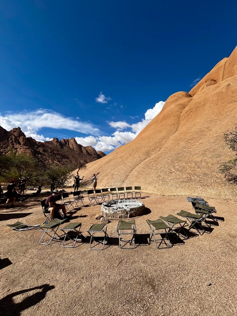       Outdoor activity area with chairs and a fire pit against large rock formations.
  