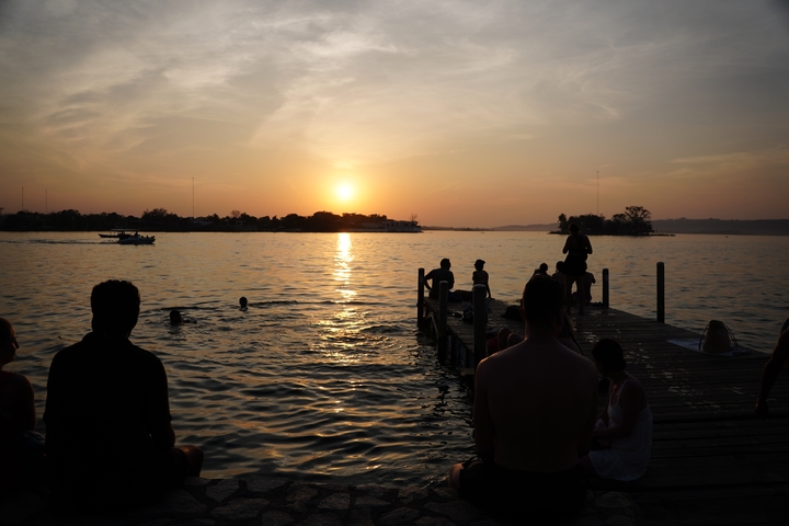 Sunset view with people swimming and a pier in the foreground.