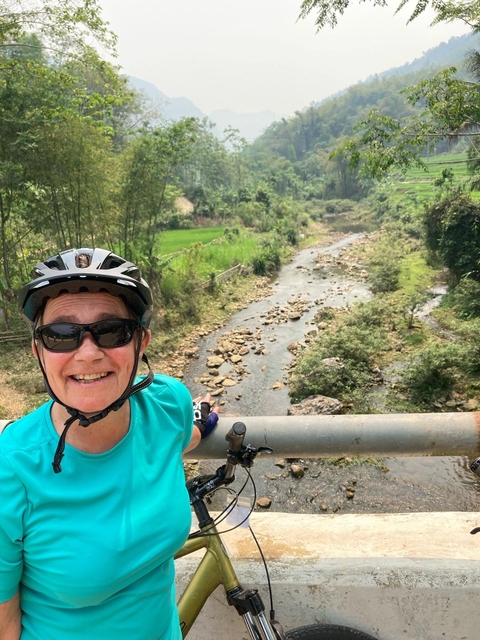 Woman cycling on a path with a lush green valley view.