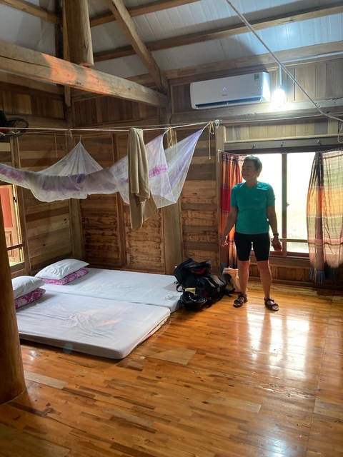 Woman in a simple accommodation with an open window and wooden interior.