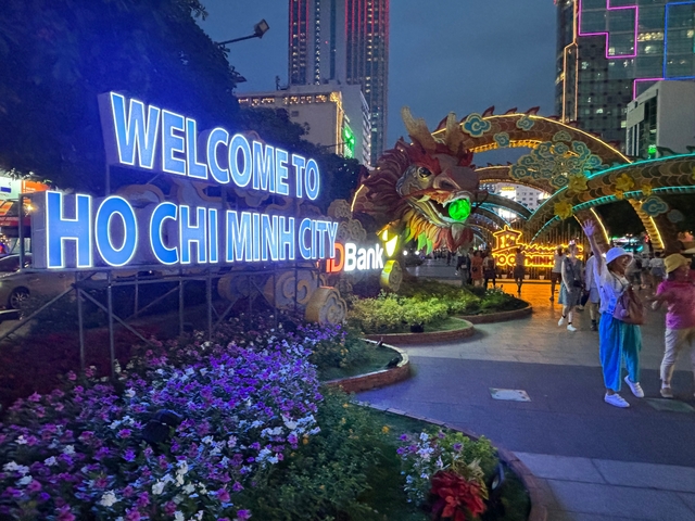 Street scene in the evening with 'Welcome to Ho Chi Minh City' sign.
