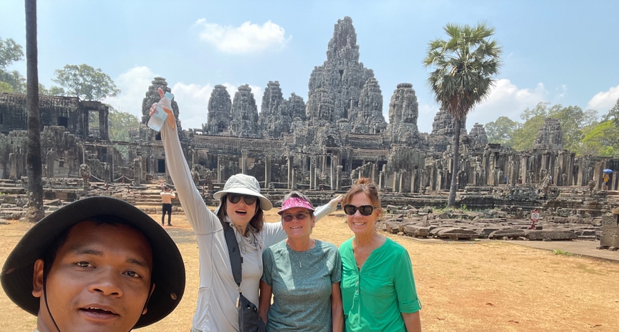 Tourists smiling with the Bayon Temple in the background.