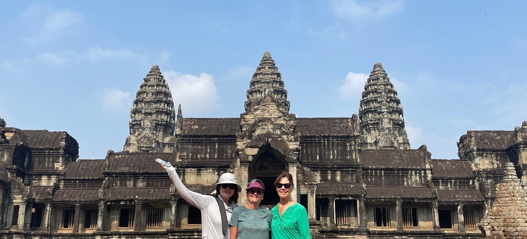 Tourists smiling in front of Angkor Wat temple.