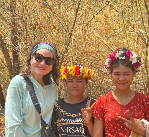       Three people posing with flower crowns in a rural setting.
  