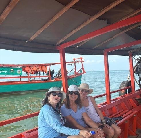       Three women posing on a boat with a colorful background.
  