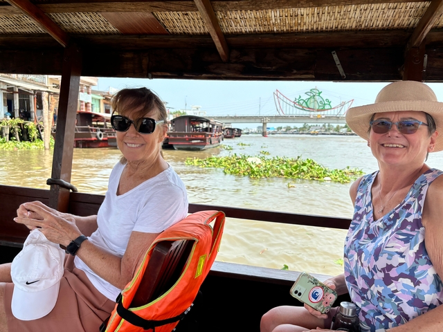 Two women sitting on a boat with a view of a river and bridge.