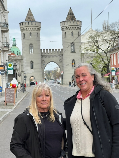 Two women standing by a street leading to a historical archway.