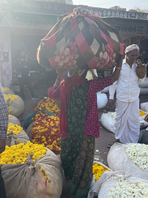       Market scene with people and bags of flowers.
  
