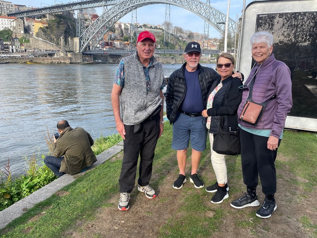       Group of people by a river with a bridge and historic cityscape.
  