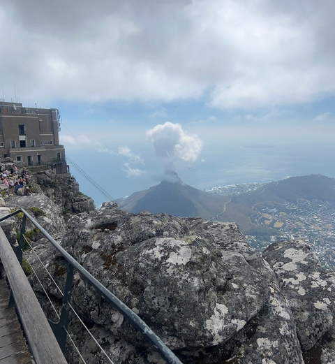       View from a mountain with a cloud over a peak and ocean visible.
  