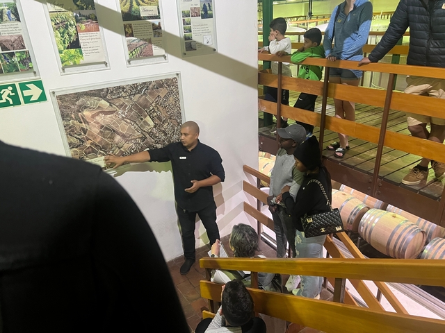       People attending a lecture in a winery, discussing wine map.
  