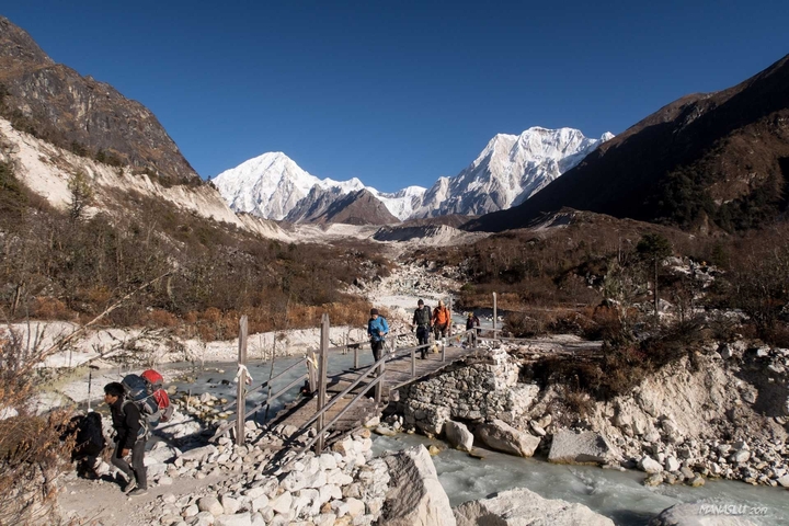 Group of hikers crossing a wooden bridge in a mountainous area.