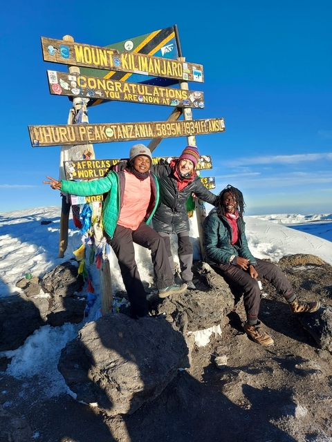       Group of people posing at a summit sign in snowy terrain.
  