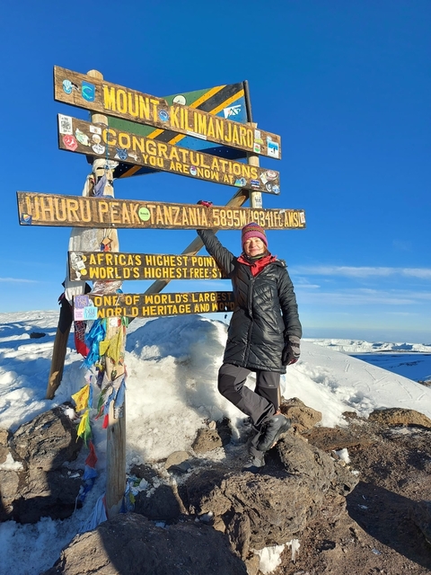       Person posing at Uhuru Peak sign in snowy conditions.
  