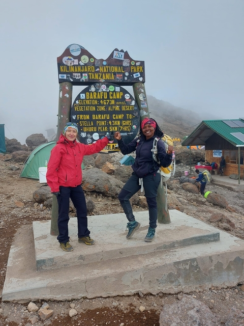       Two women posing in front of a camp sign with tents around.
  