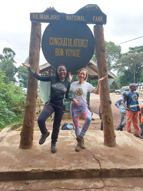       Two women joyfully posing under a sign at a campsite.
  