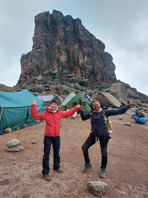       Two women holding hands in front of tents and rocky terrain.
  