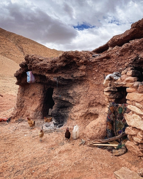 Rustic dwelling built into a rock formation with chickens outside.