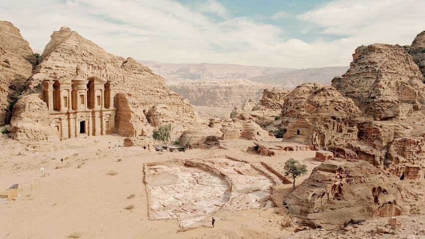 Ancient rock-hewn monastery in Petra surrounded by rocky landscape.
