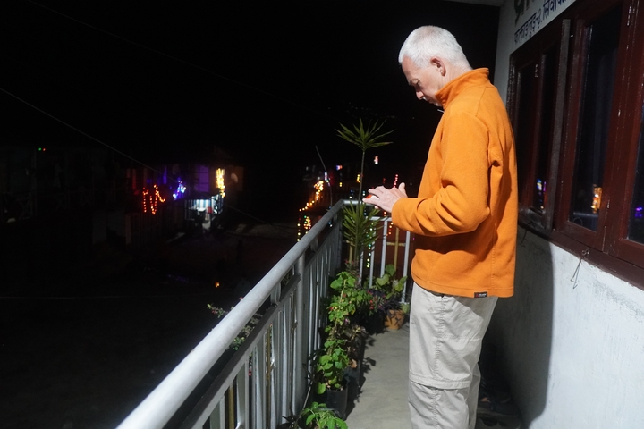       Man on a balcony with night view and distant lights.
  