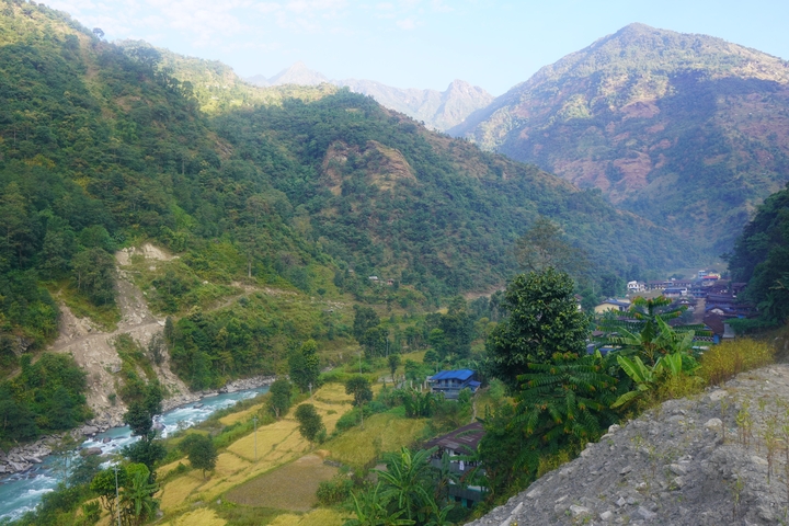       A scenic view of a valley with a river, fields, and houses, surrounded by mountains.
  