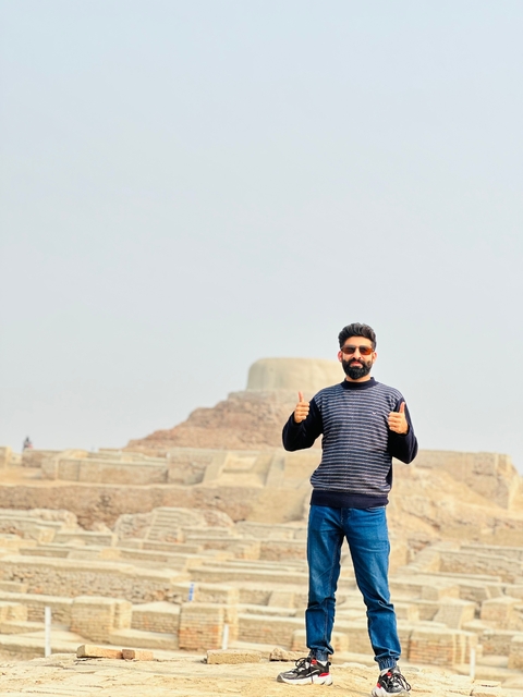       A person posing with thumbs up in front of an ancient ruin.
  