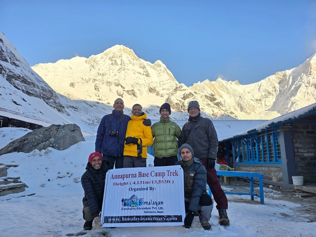 Group posing with a sign at Annapurna Base Camp covered in snow.