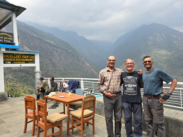 Three people posing at a restaurant terrace with a view of mountains.