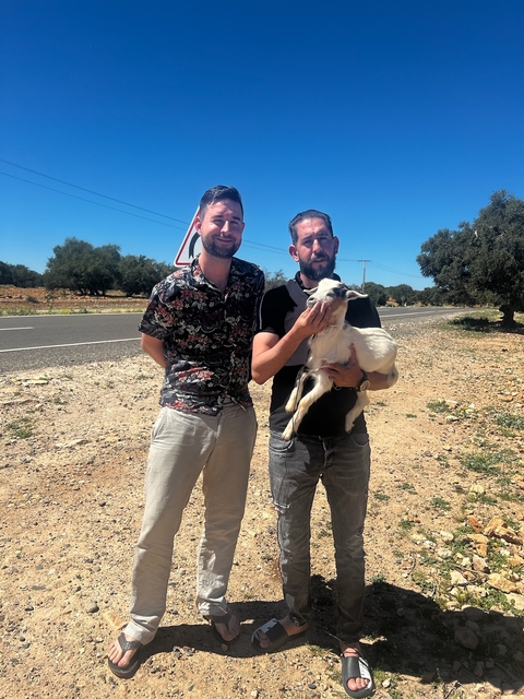 Two men with a goat by the roadside.