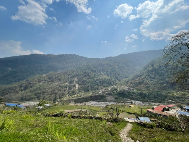 Green terraced fields in the valley with scattered houses under a blue sky.