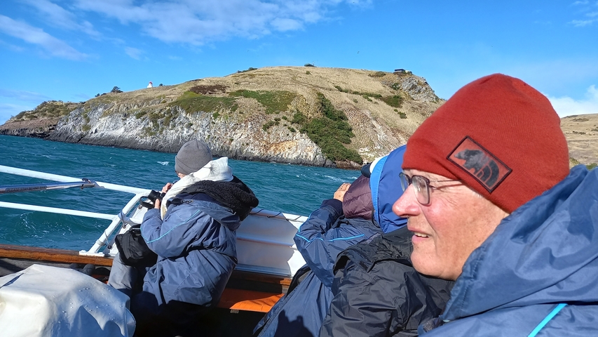 People in outdoor winter gear on a boat near a rocky coast.